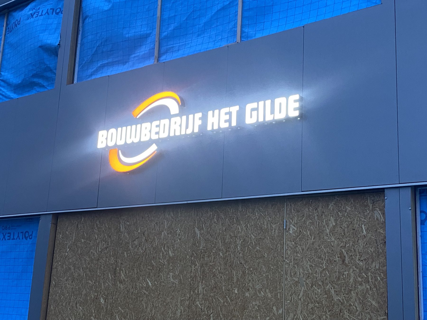 Verlicht logo van Bouwbedrijf het Gilde op de gevel